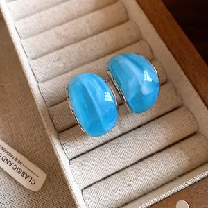 Primer plano de pendientes de resina azul en forma de C con textura de mármol en joyero