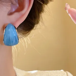 Detalle de un pendiente de resina azul en forma de C en la oreja de una modelo.