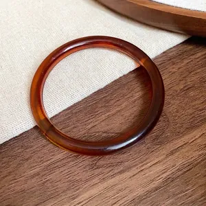 Vintage amber tortoiseshell acetate bangle bracelet on a rustic wood and linen background.