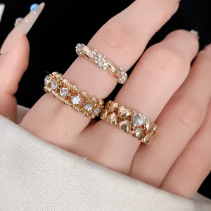 Dettaglio di tre anelli dorati con cuori e strass indossati su una mano.