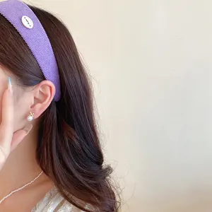 Dettaglio di un cerchietto in tessuto testurizzato viola con un piccolo bottone ovale