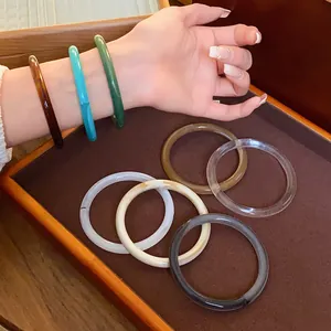 Close-up detail of vintage acrylic acetate bangles in various colors on hand and wooden tray