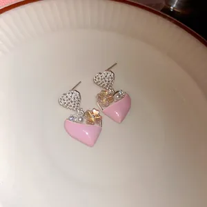 Detailopname van zilveren naald oorbellen met roze hart, kristal en bloemaccenten.