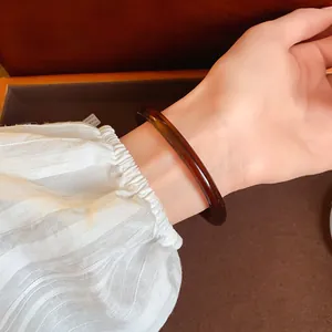 Close-up of a vintage amber acetate acrylic bangle worn on a wrist with white striped sleeve