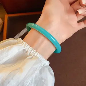 A detailed macro view of a stylish green acrylic acetate bangle worn on a female wrist