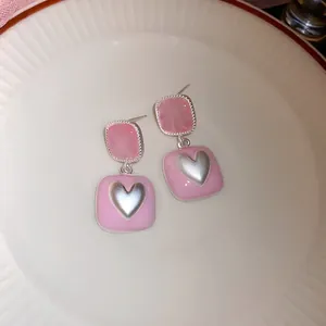 Close-up van zoete roze vierkante oorbellen met zilveren hart op een wit bord