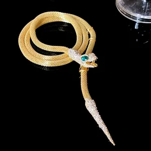 Detailed macro view of a gold snake necklace with crystal-set head and green stone eyes.