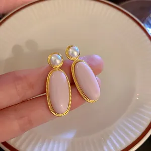 Detailweergave van vintage roze ovale oorknopjes met parelaccenten en gouden rand.