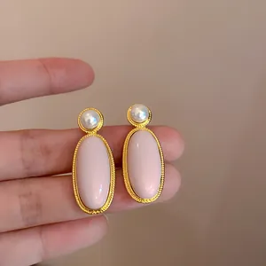 Vintage roze ovale oorknopjes met pareldetail vastgehouden tegen een beige achtergrond