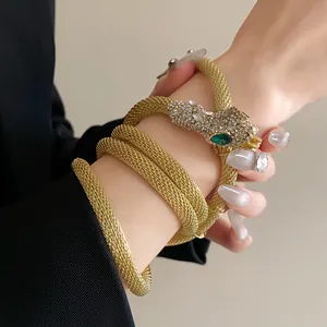 Close-up detail of a sparkling gold mesh snake bracelet with green stone eyes