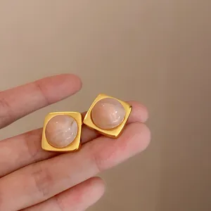 Macro-opname van elegante vierkante gouden oorknopjes met roze marmeren harsinleg