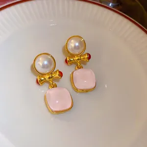 Detailopname van elegante gouden strikoorbellen met roze stenen en parels op een bord