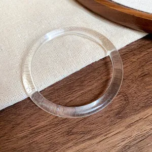 Close-up of a clear wide-band acrylic bracelet on a rustic wood and fabric background