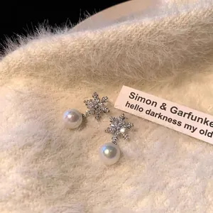Close-up of snowflake-shaped pearl earrings on a soft cream sweater background