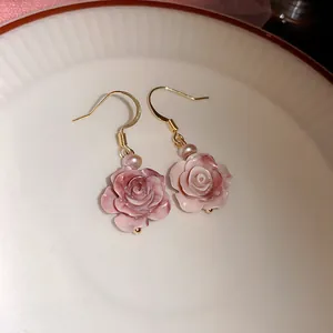 Detail van verfijnde roze rozenoorbellen met elegante gouden haken en een mooie parel