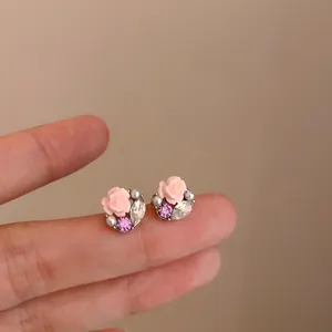 Detailopname van roze bloem oorbellen met paarse strass steentjes op vingers voor maat