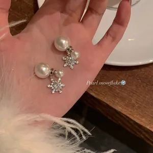Detailed macro view of snowflake pearl earrings held in hand for close inspection.