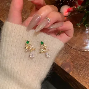 Detailed view of sparkling Christmas tree stud earrings with pearls pinned on a cozy knit sweater.