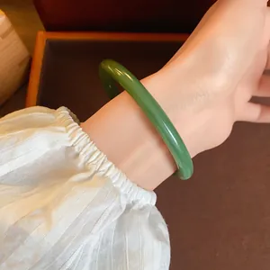Detailed view of an elegant green acetate bangle bracelet worn on a wrist with white sleeve