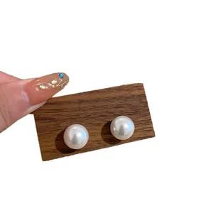 Elegant white pearl stud earrings with silver needles on a wood display card