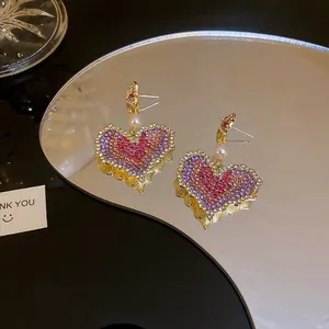 Detail view of heart-shaped earrings with purple gradient rhinestones and small pearls
