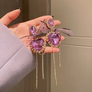 Macro detail of purple heart-shaped rhinestone earrings with long tassels and mesh bows.