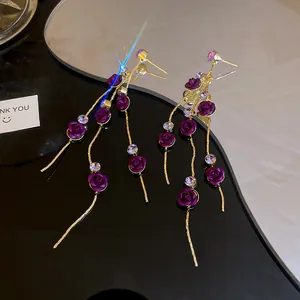 Detail view of purple rose dangle earrings with gold tassels and crystal accents.