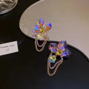 Detailed macro view of purple iridescent flower earrings with golden chain tassels.