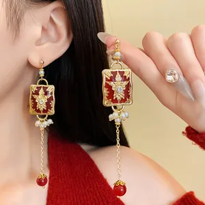 Macro view of vintage style gold-tone drop earrings with red enamel and pearl details.
