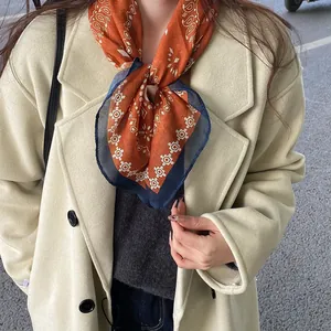 Close-up of a vintage orange paisley scarf styled with a beige winter coat for women.