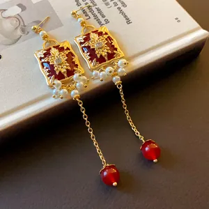 Close-up of vintage red enamel flower earrings with pearls and long gold chains.