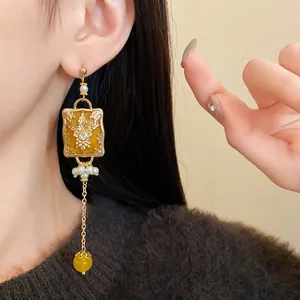 Close-up of a vintage-style gold long earring with flower pattern and yellow bead.