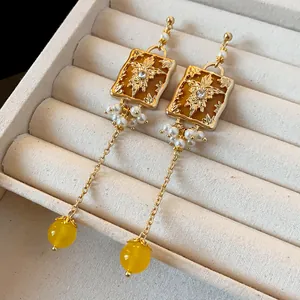 Close-up of vintage gold-tone earrings with floral relief, pearls and yellow beads.