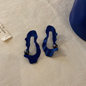 Close-up of Klein blue irregular wavy matte earrings with dark pearl on linen background
