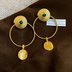 Detail shot of vintage style gold textured hoop earrings with green stones on brown velvet