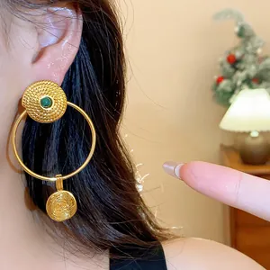 Close-up of vintage gold-plated round earrings with wrinkled texture and green stone.
