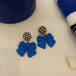 Close-up of Klein blue bow earrings with houndstooth pattern and silver needles.