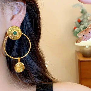 Close-up of vintage gold hoop earrings with textured round pendants and green gemstones