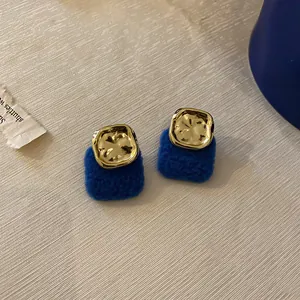 Detail of Klein blue textured earrings with irregular gold metal square accent on fabric.