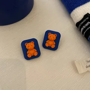 Close-up view of retro Klein blue square stud earrings featuring cute orange bear figurines