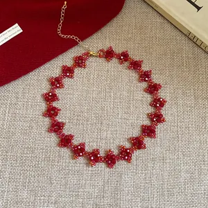 Macro view of handmade red flower beaded choker with adjustable gold extender chain on rustic background