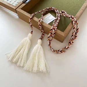Close-up of bohemian braided belt with elegant white tassels on a vintage wooden box