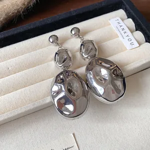 Close-up macro view of silver tone drop earrings with a crumpled oval metallic texture