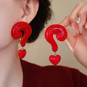 Close-up view of creative red question mark earrings with heart pendants on model