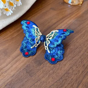 Dettaglio macro di un anello a farfalla ricamato blu con strass rossi e montatura dorata