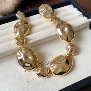 Close-up detail of a chunky gold necklace featuring unique pleated oval metal links