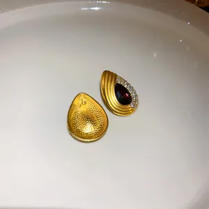 Détail de boucles d'oreilles vintage en goutte d'or avec cristal rouge et strass.