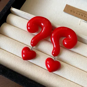 Close-up of glossy red question mark earrings with heart charms in a jewelry box