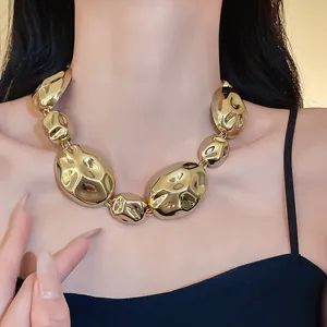 Close-up of a chunky gold choker necklace with irregular crumpled oval bead design.
