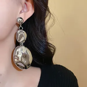 Detailed close-up view of a metallic crumpled oval drop earring worn by a female model